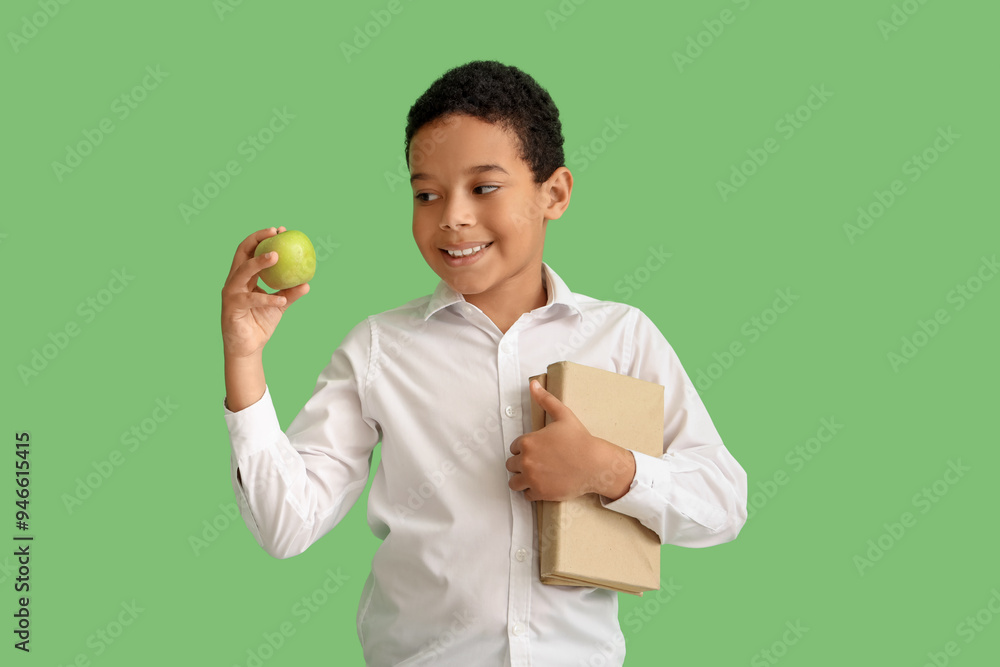 Wall mural Little African-American schoolboy with books and apple on green background