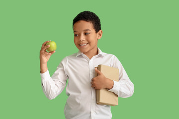Little African-American schoolboy with books and apple on green background