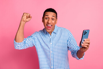 Photo of lucky positive guy dressed checkered shirt winning game modern device emtpy space isolated pink color background