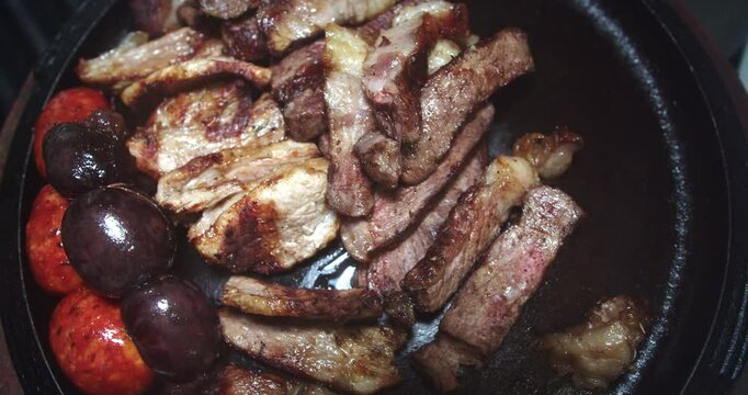 Beautiful slow motion shot of chunks of meat being placed on a grill plate with sausages, sliced loin and potatoes inside a restaurant kitchen.