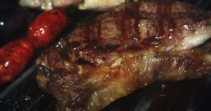 Beautiful slow motion close-up shot of different types of beef and pork with chorizo ​​and blood sausage on a charcoal grill inside a restaurant kitchen.