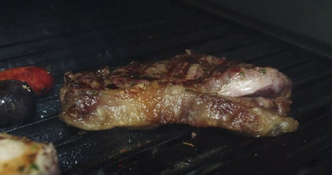 Beautiful slow motion shot of a pork chop being handled with tongs inside a grill to be cooked while smoking in a restaurant kitchen.