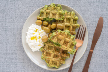 Belgian waffles served with green olives and cottage cheese on ceramic plate. Top view.
