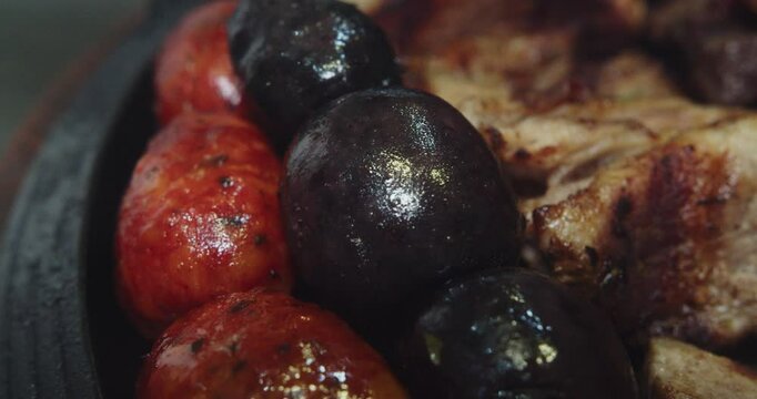Beautiful slow motion close-up shot of a strip of chorizo and blood sausage placed on a Venezuelan grill plate in a restaurant kitchen.
