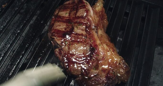 Beautiful slow motion shot of a pork loin being moistened with stew and fat with a brush on a grill inside a kitchen.