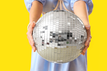 Fashionable young woman with disco ball on yellow background