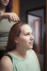 A woman with red hair is getting her hair done by another woman