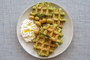 Belgian waffles served with green olives and cottage cheese on ceramic plate. Top view.