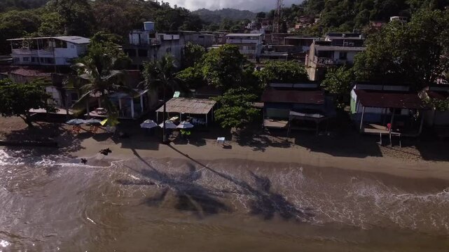 The camera pulls back, showcasing a panoramic view of the coast, from the beach and town to the interior of the forest.