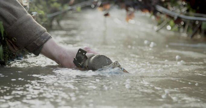 A hand lowering a canteen into a stream, World War 2 Reenactor, Static Shot