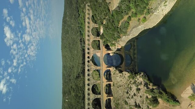 Vertical wide shot of Aqueduc de Roquefavour Bridge in France with clear river. Green Mountains and blue sky in summer.
