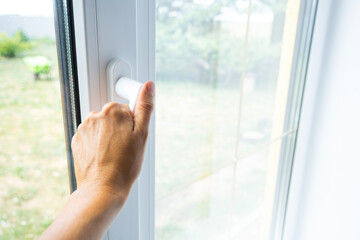 The hand holds the handle of a plastic double-glazed window, closing and opening the window with a rotary mechanism, the position of the handle for ventilation, micro-ventilation