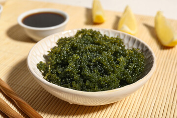Bowl with healthy seaweed, soy sauce and lemon slices on bamboo mat, closeup