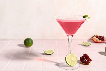 Glass of Cosmopolitan cocktail with lime and pomegranate on pink tile table