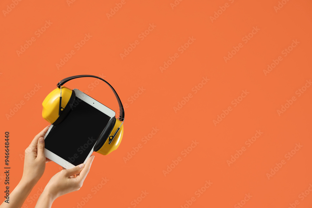 Wall mural woman with blank tablet computer and hearing protectors on orange background