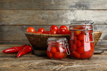Jars of pickled tomatoes on wooden background