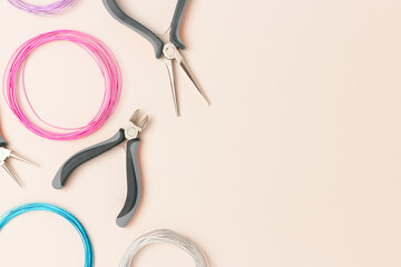 Aluminum multicolored wire and tools for jewelry making scattered on a beige background.
