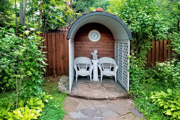 A white summer gazebo with a wicker chairs in the garden.
