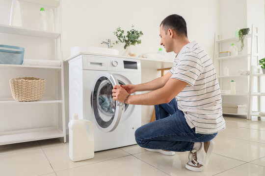 Young man putting capsule of detergent into washing machine in laundry room - Powered by Adobe