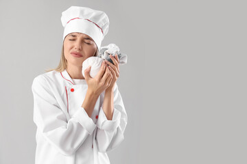 Young female chef with ice pack suffering from tooth ache on grey background