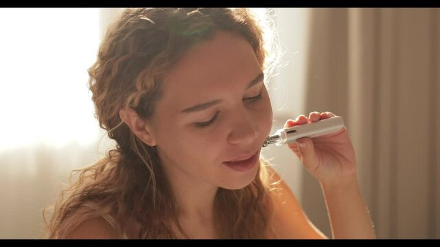 A girl of natural beauty provides skin care. Uses a Microcurrent facial massager at home and smiles