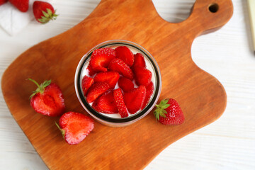 Glass of tasty yogurt with fresh strawberries on white wooden background