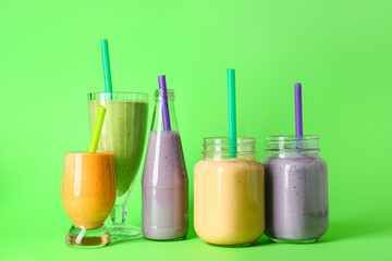 Glasses and mason jars of different fresh smoothie on green background