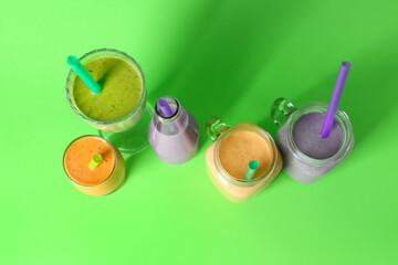 Glasses and mason jars of different fresh smoothie on green background
