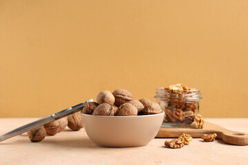 Bowl with tasty walnuts and nutcracker on beige background