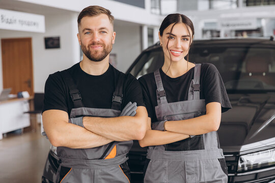 Auto car repair service center. Two happy mechanics - man and woman standing by the car