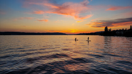 Sunset on the lake Constance. Silhouettes of two people on Stand Up Paddle Board. Water sports.