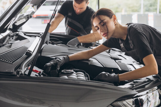 Trying to identify the source of the problem. Two mechanics man and woman working together at open hood on a car in an auto repair shop.