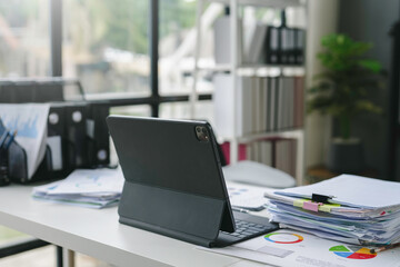 Modern office desk with a tablet computer showing financial reports and paperwork, suggesting a busy work environment