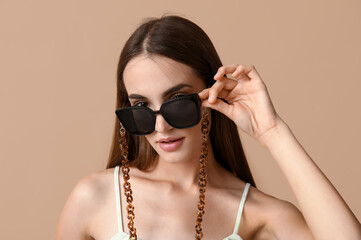 Beautiful young woman in stylish sunglasses on brown background