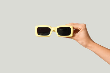 Female hand with stylish yellow sunglasses on grey background