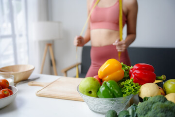 Woman is holding a measuring tape around her waist with a bowl of fresh vegetables in the foreground