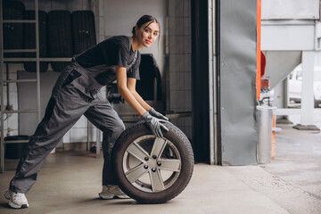 Smiling Charming Woman Car mechanic holding tire at repair garage. Replacement of winter and summer tires.