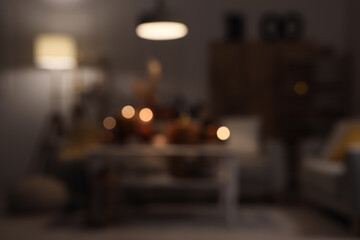 Blurred view of dark living room decorated for Halloween with glowing lamp, sofas and table at night