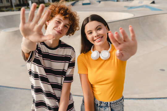 Couple of happy friends teenagers boy and girl classmates high school pupils students in colorful t-shirts holding hands up celebration summer vacation looking at camera in skate park