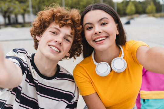 Positive couple of teenagers friends classmates students school pupils taking picture of themselves for selfie with smart mobile phone sitting spend time together in skate park ramp after lessons - Powered by Adobe