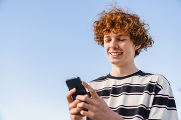 Smiling redhead caucasian curly teen school boy guy teenager skater in casual clothing holding...