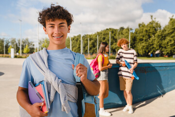Handsome curly teen high school boy guy with braces bag in casual clothes holding netbooks...