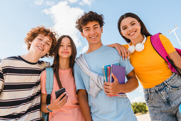 Close up photo of friends teenagers high school pupils college students with bags holding books phone gadgets spending time meeting hanging out outside in skate green nature park looking at camera