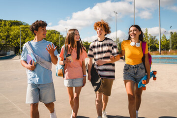 Multiethnic friends students guys girls hanging outside on a sunny day having fun walking on city street urban nature park. Group of young people enjoying summer vacation together. Friendship concept