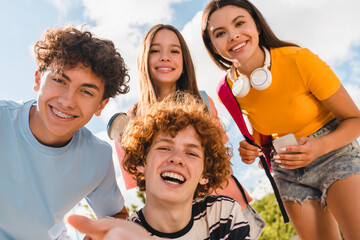 Group of positive teenagers high school pupils friends classmates college students boys girls with bags taking selfie shot having fun handing out meeting outside in urban street sport yard court park
