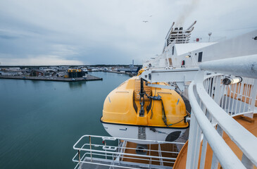 Norwegian ferry with its bright yellow rescue boat securely attached, cruising through calm harbor....