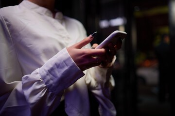 Woman in stylish dress with chic manicure using smartphone in closeup shot in nightclub
