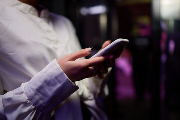 Woman in stylish dress with chic manicure using smartphone in closeup shot in nightclub