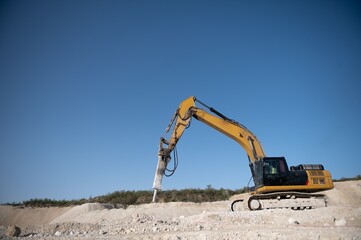 heavy organge excavator with shovel standing on hill with rocks