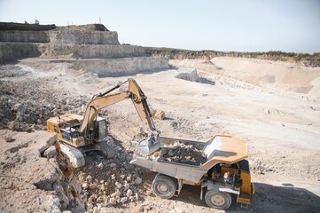 Large quarry dump truck. Big yellow mining truck at work site. Loading stone into body truck